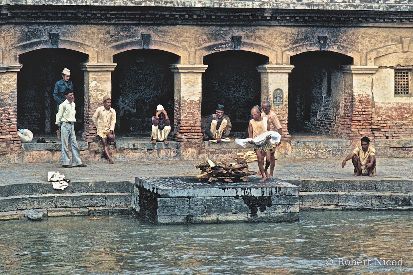 Nepal 1977 — Funeral preparations for an eight-year-old child. On the right, his father squatting, eyes on the ground, Pashupatinath 1977